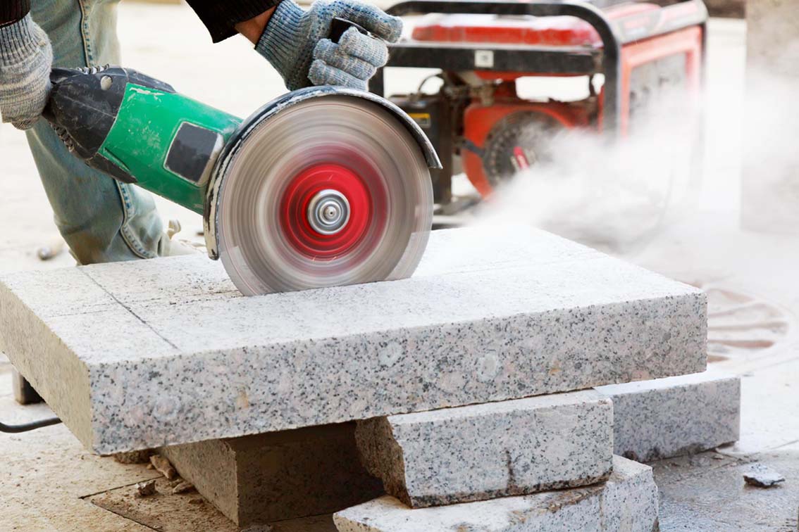 closeup-of-worker-cutting-granite-slab-with-grinder-dust-while-grinding-stone-pavement